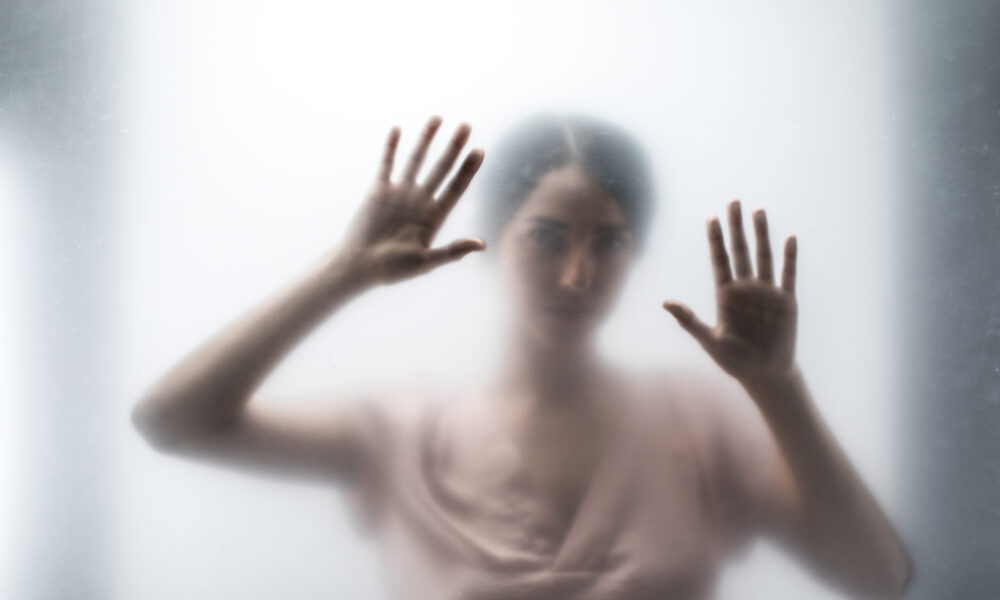 Silhouette of woman looking through the glass and touching it with hands